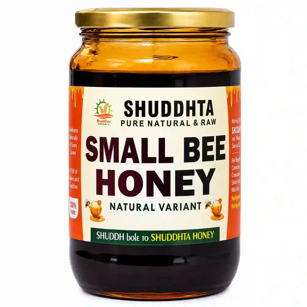 A glass jar of Shuddhta Small Bee Honey with a gold metal lid and a white label with orange side panels, set against a plain white background.