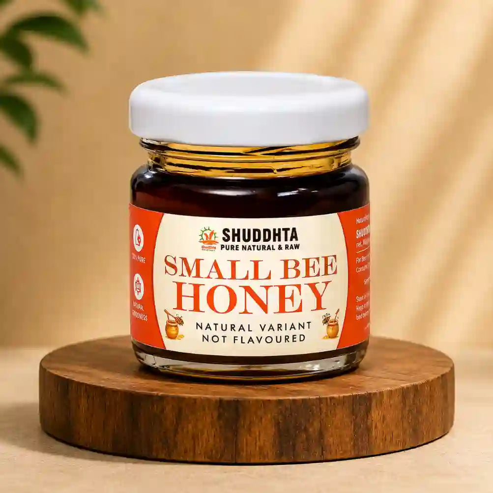 A jar of Shuddhta Small Bee Honey, not flavoured, displayed on a round wooden coaster against a warm beige background with soft leaf shadows.