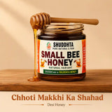 A jar of Shuddhta Small Bee Honey sits on a wooden surface with honey dripping from a wooden honey dipper. The background is a warm beige with soft shadows, and text below reads 'Chhoti Makkhi Ka Shahad' and 'Desi Honey'.