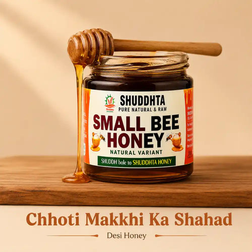 A jar of Shuddhta Small Bee Honey sits on a wooden surface with honey dripping from a wooden honey dipper. The background is a warm beige with soft shadows, and text below reads 'Chhoti Makkhi Ka Shahad' and 'Desi Honey'.