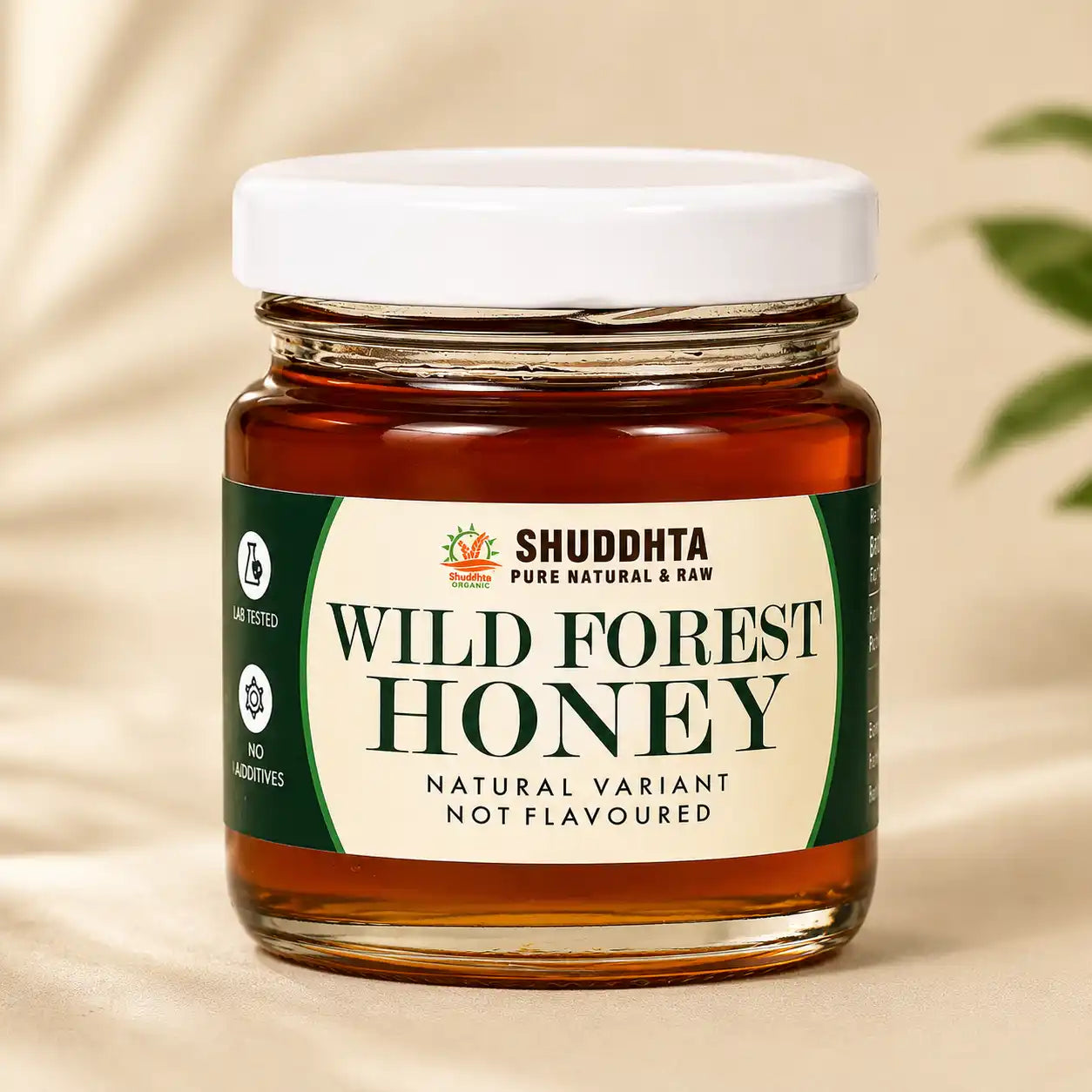 A glass jar of Shuddhta Wild Forest Honey with a white lid and cream label, set against a warm beige background with soft leaf shadows.